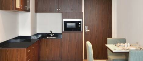 Cocina compacta con armarios de madera, encimera negra y microondas integrado. Hay un comedor con mesa y dos sillas.
