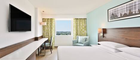 A hotel room with a bed, a desk, a chair, a TV, and a window with curtains.