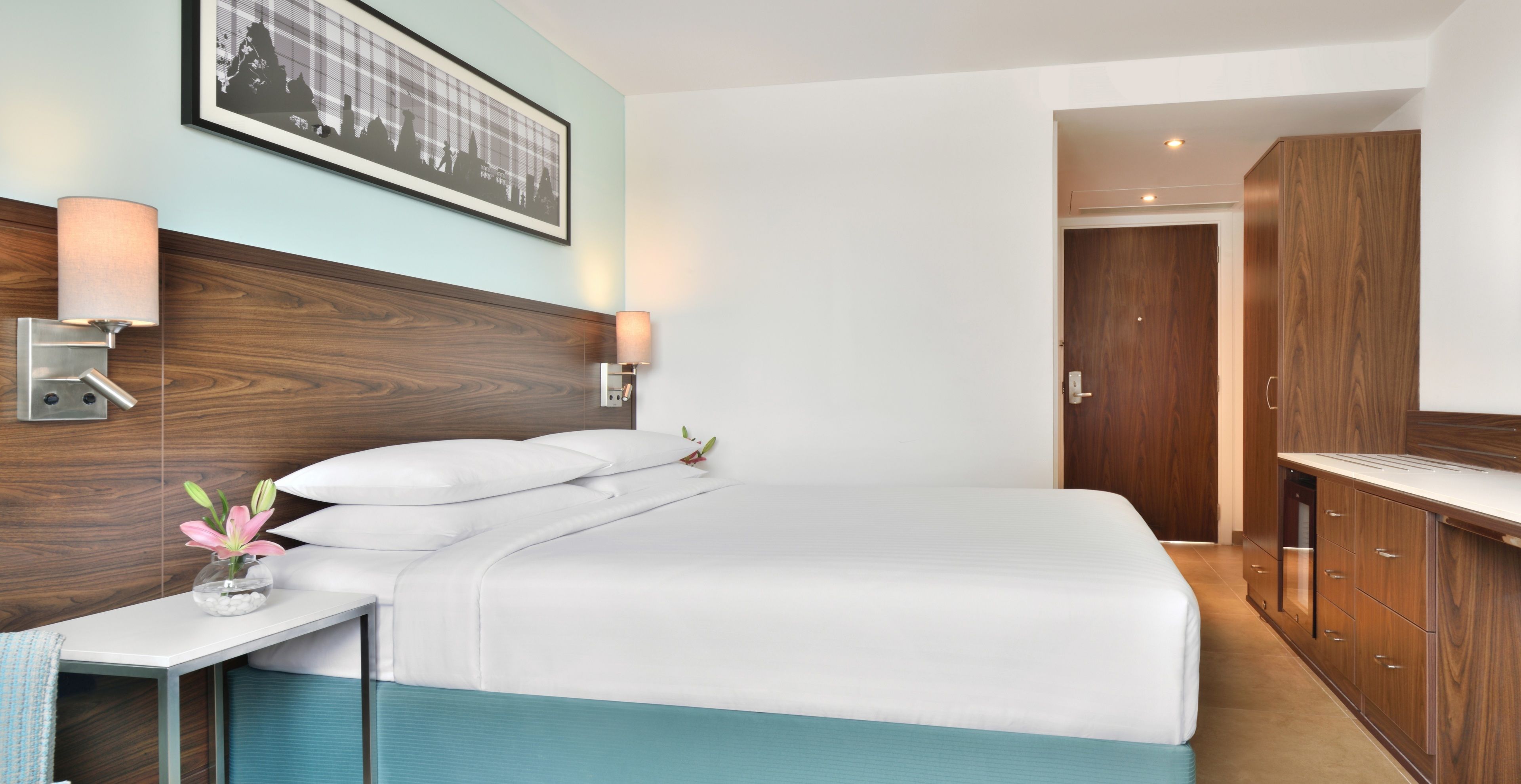 A hotel room with a bed, bedside tables, a lamp, a framed picture on the wall, and a wooden wardrobe.