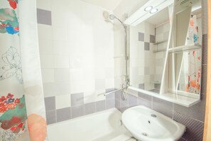 Bathroom features a bathtub, sink, and showerhead, with a mirror and glass shelf.