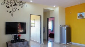 A modern living room with a flat-screen TV, a marble coffee table, a refrigerator, and a water dispenser.