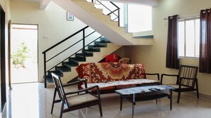 A living room with a sofa, two chairs, a coffee table, a staircase, and a window with curtains.