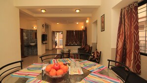 A dining area with a glass table, colorful tablecloths, and a bowl of fruit.