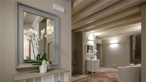 A hotel room with a large mirror, a vanity with a vase of flowers, a white dresser, a small table with a vase, a decorative mirror, and a patterned rug. - Locanda in Borgo Garni & Wellness (Borgo Valsugana)