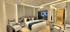 A modern hotel room with a large bed, two armchairs, a nightstand, a vanity with a mirror, and a window with a view of the city. - Hotel Mansarover Paradise (Moradabad)