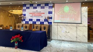 Montaje para una conferencia con un cartel para el CME en colaboración con la Asociación de Cirujanos de Moradabad, una mesa con botellas de agua y un arreglo floral.