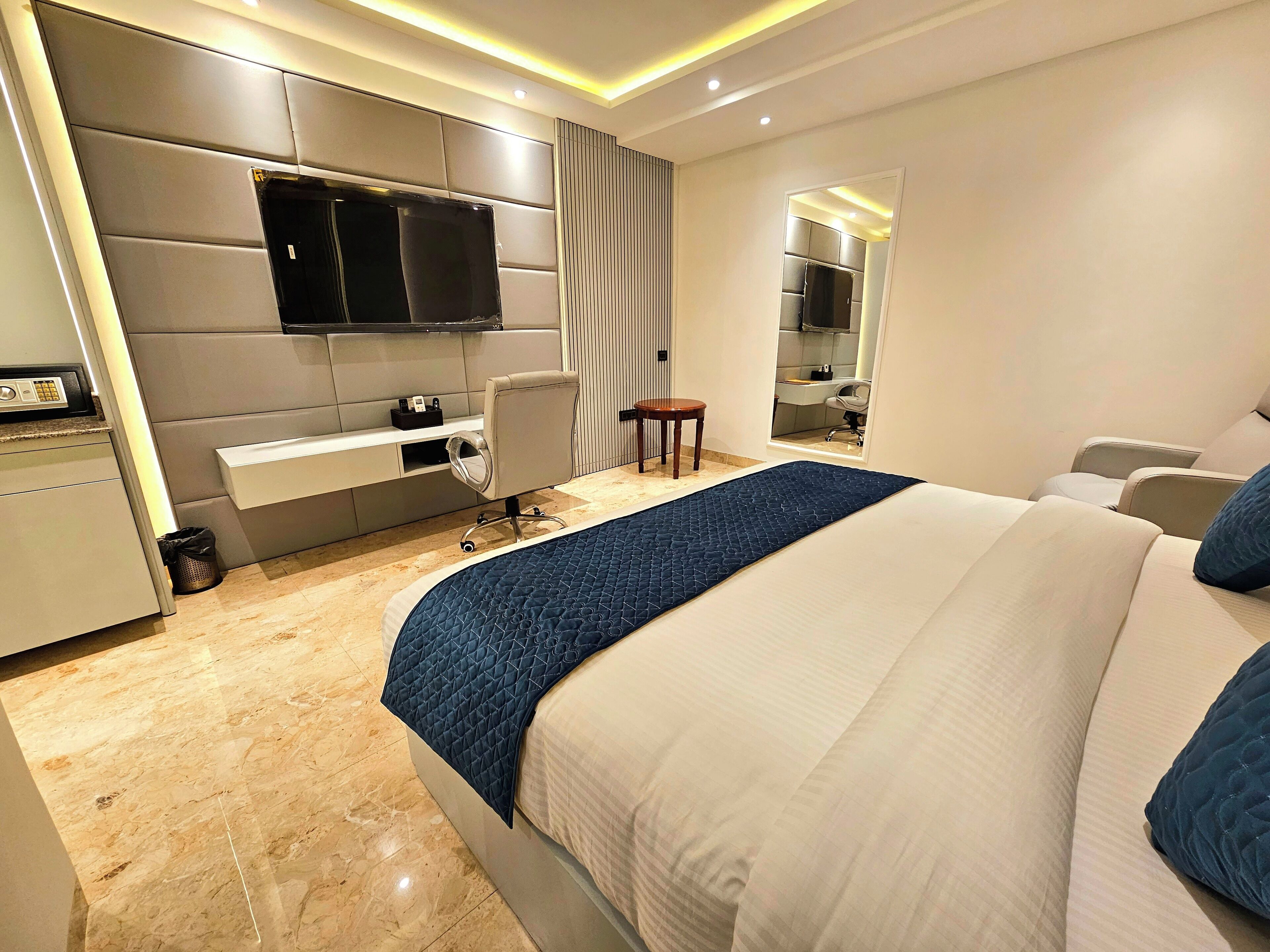 A modern hotel room with a large bed, a desk, a chair, and a TV mounted on the wall.