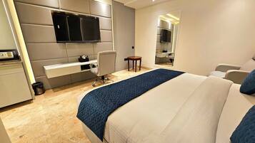 A modern hotel room with a large bed, a desk, a chair, and a TV mounted on the wall.