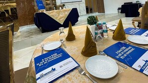 Un salón de conferencias con una pantalla grande, mesas redondas con posavasos azules y una araña.