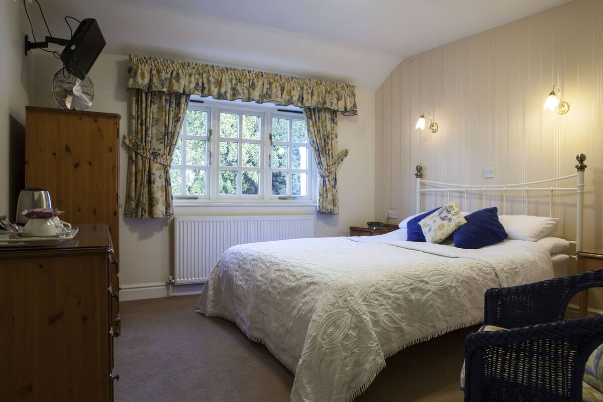 A bedroom with a large bed, a dresser, a window with curtains, and wall-mounted lights.