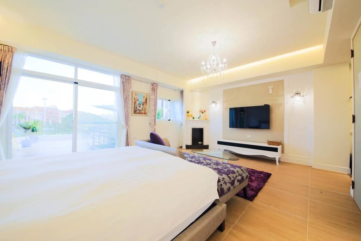A modern bedroom with a large bed, a TV, and a fireplace.