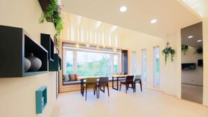 A spacious room with a large window, a built-in bench, and a dining area with chairs.