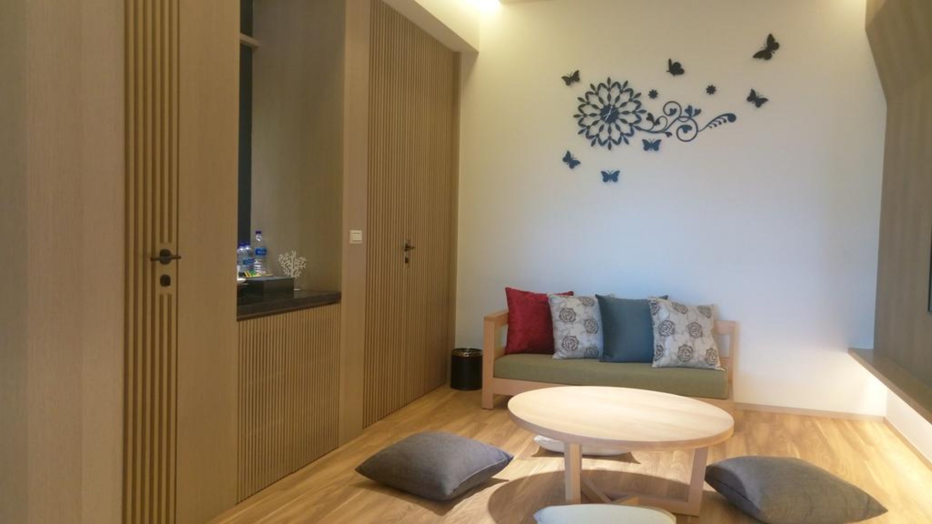 Una habitación moderna con un armario de madera, un sofá con cojines estampados, una mesa redonda de madera y decoración de pared que incluye mariposas y un diseño floral.