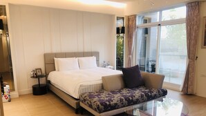 A bedroom with a bed, a sofa, a glass coffee table, and a large window with curtains.