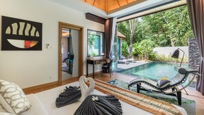 A modern room with a wooden ceiling, a large window overlooking a pool, a sofa, a desk, and a lounge chair by the pool. - Inspire Villas Phuket (Rawai)