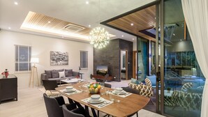A modern living room with a dining area, large windows, and a view of the outdoors. - Inspire Villas Phuket (Rawai)
