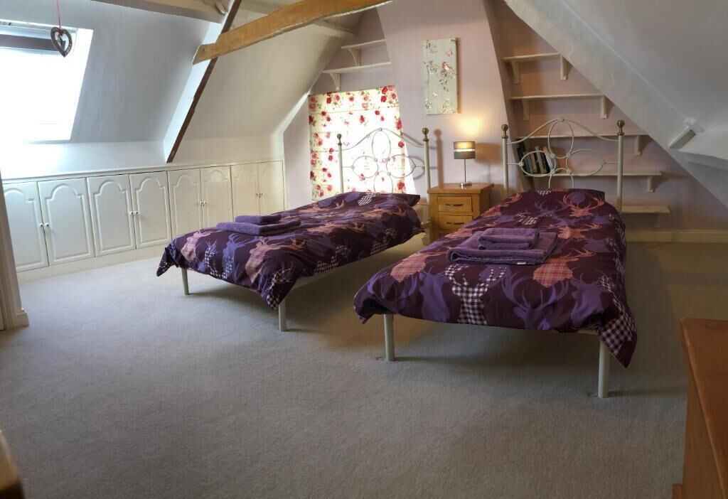 A bedroom with two single beds, a window with a heart-shaped decoration, a staircase, and a small bedside table with a lamp.