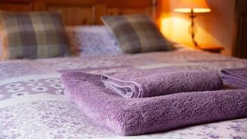 A neatly made bed with purple towels, plaid pillows, and a lamp in the background.