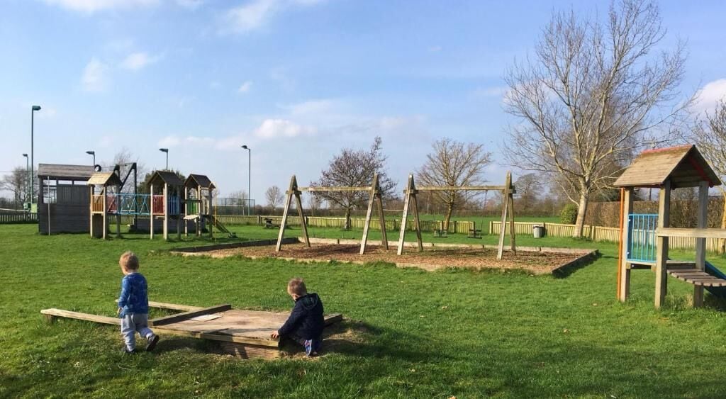 Une aire de jeux avec des balançoires, un toboggan et un petit abri.