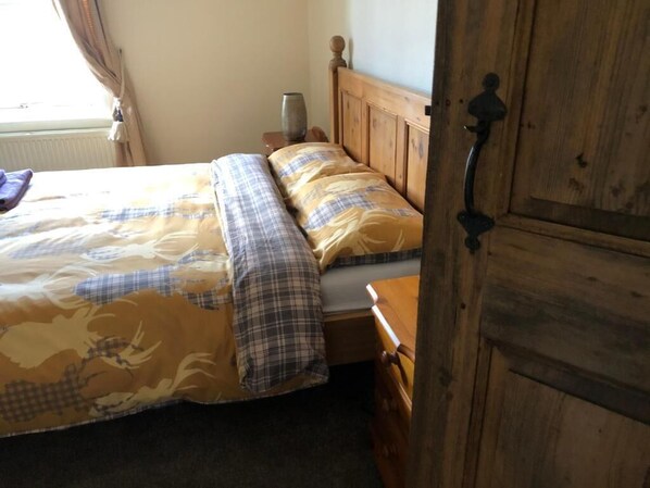 A bed with a plaid bedspread, a wooden headboard, and a nightstand with a lamp. - Ceilidh Cottage (York)