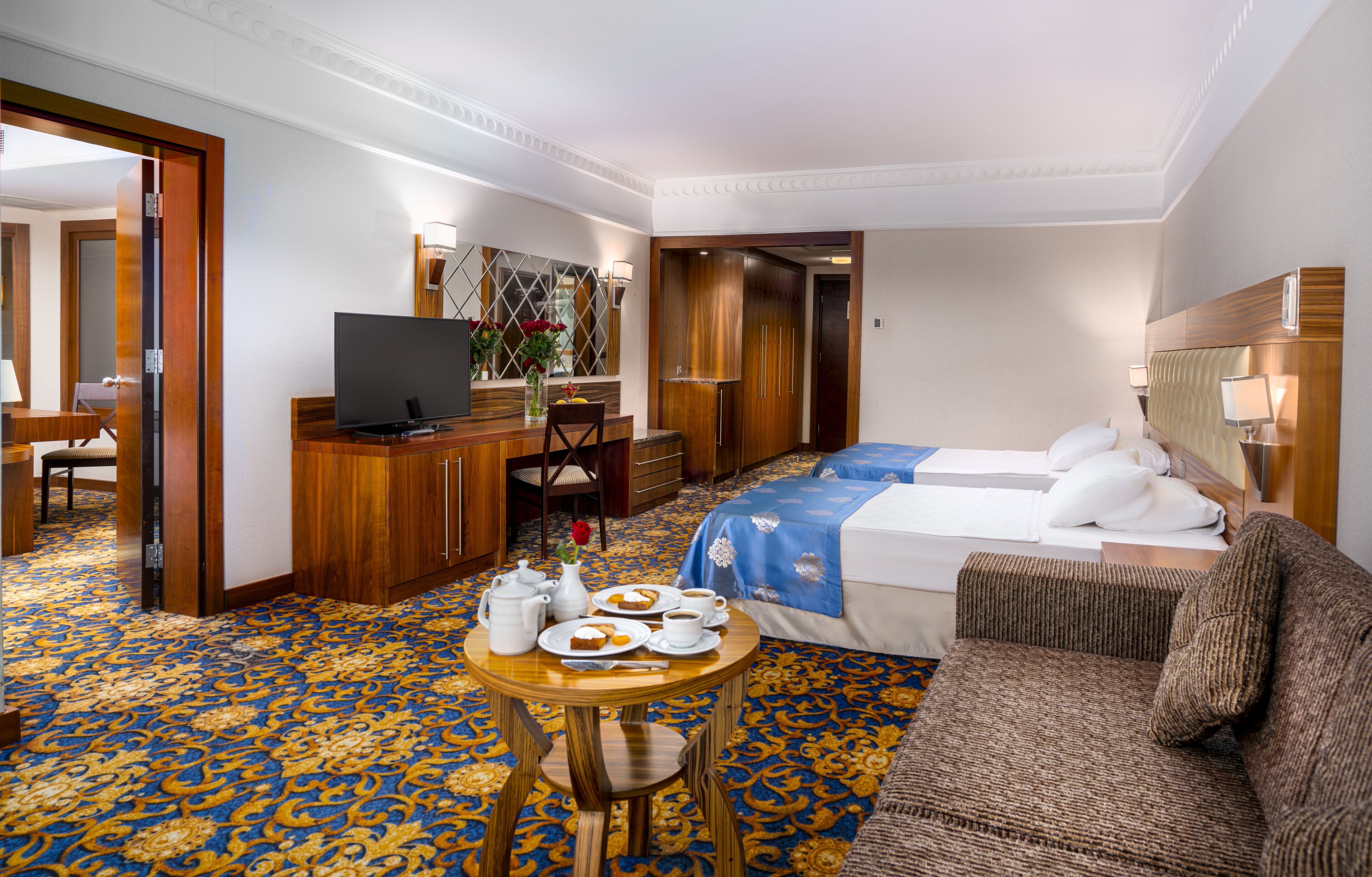 A hotel room with a bed, a sofa, a dining table with breakfast, a TV, and a desk.