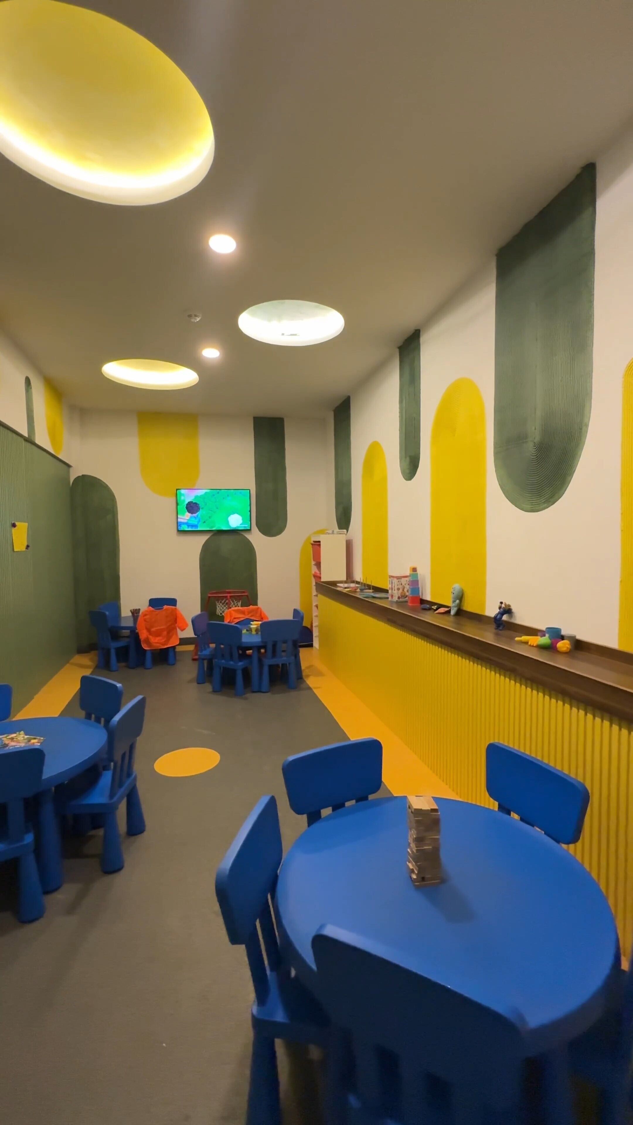 A children's play area with blue tables and chairs, a basketball hoop, and a television mounted on the wall.