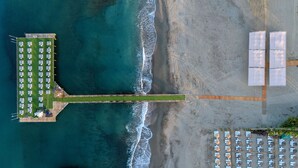 Vista aèria d'un complex turístic a la platja, amb un llarg moll, files de cadiretes i ombrel·les.