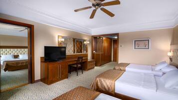 A hotel room with a bed, a desk with a television, a chair, a wardrobe, and a ceiling fan.