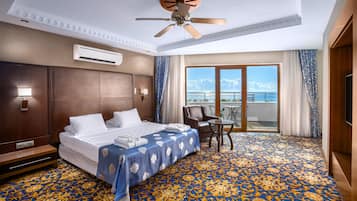 Une chambre d’hôtel dotée d’un grand lit, d’un ventilateur de plafond, d’un climatiseur, d’un balcon avec vue sur l’océan et d’une moquette à motifs.