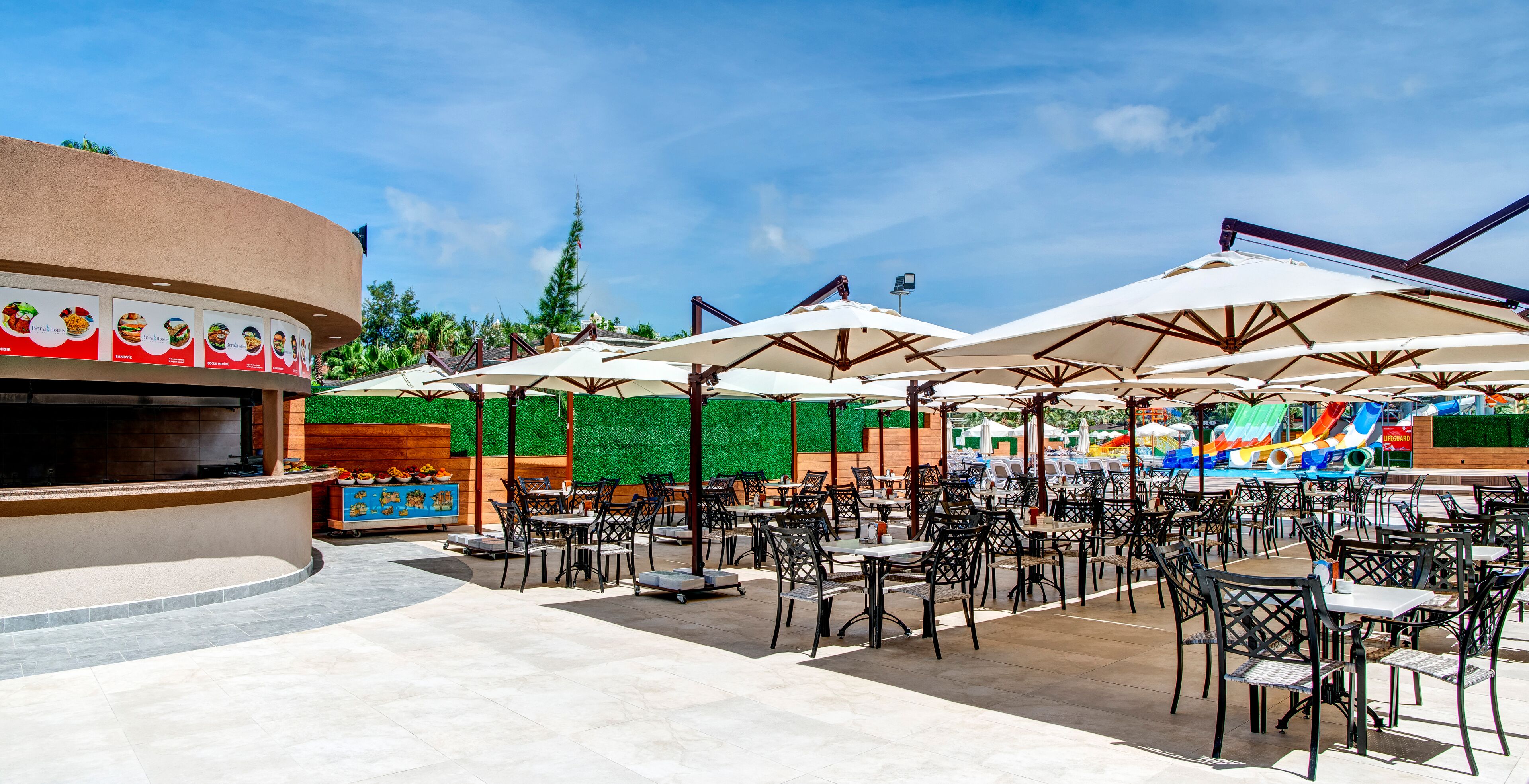 Une terrasse extérieure avec plusieurs tables et chaises, un stand de restauration et un espace piscine.