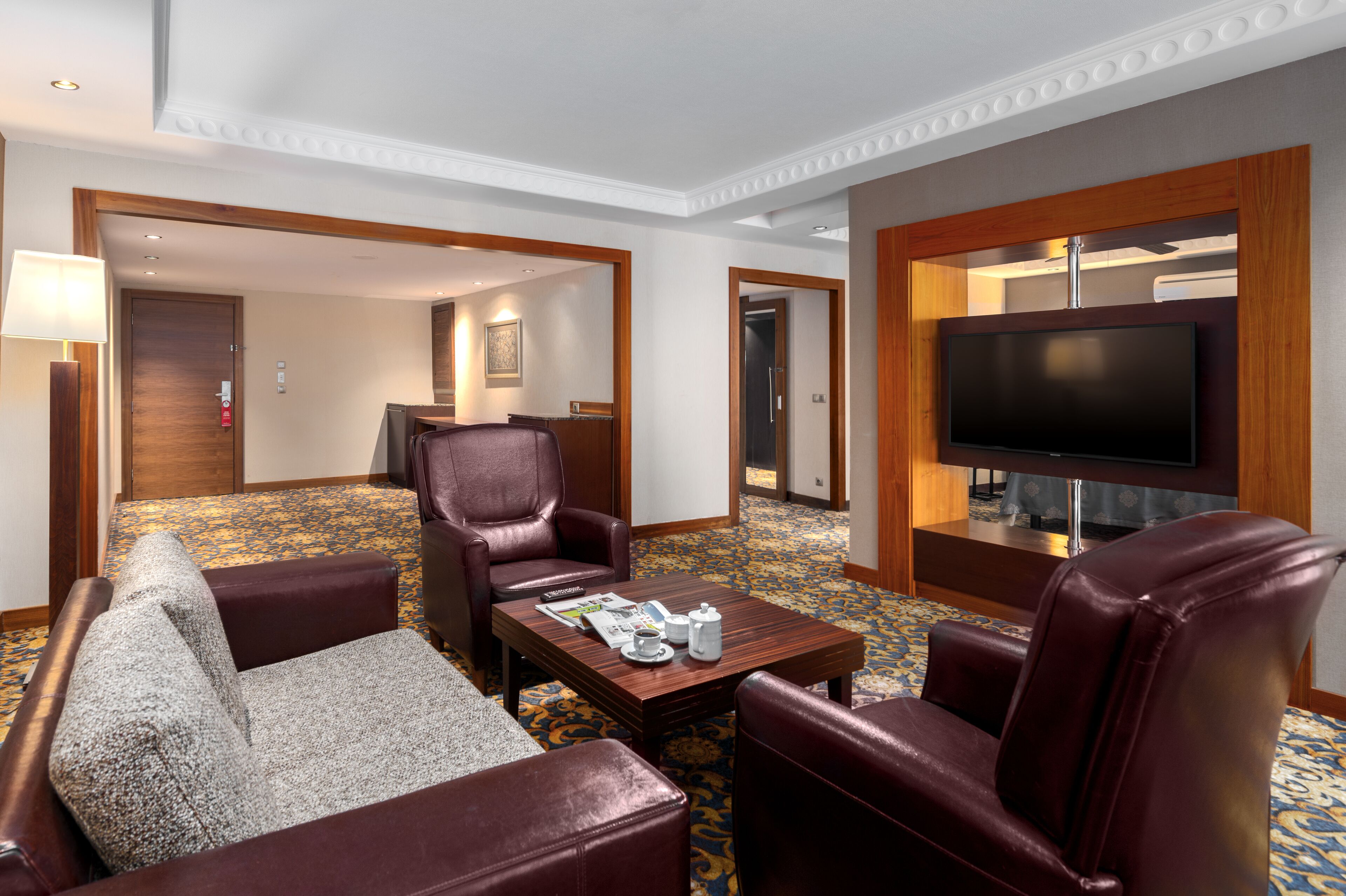 A hotel room with a large flat-screen TV, leather armchairs, a sofa, and a coffee table.