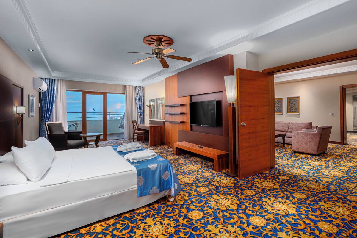 A hotel room with a bed, a TV, a desk, a chair, a sofa, and a balcony with a view.