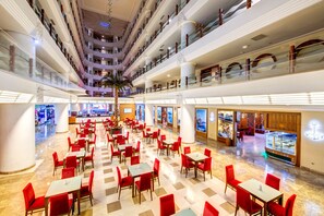Un vestíbulo de hotel de varios niveles con piso a cuadros, asientos rojos y una palmera en el centro.