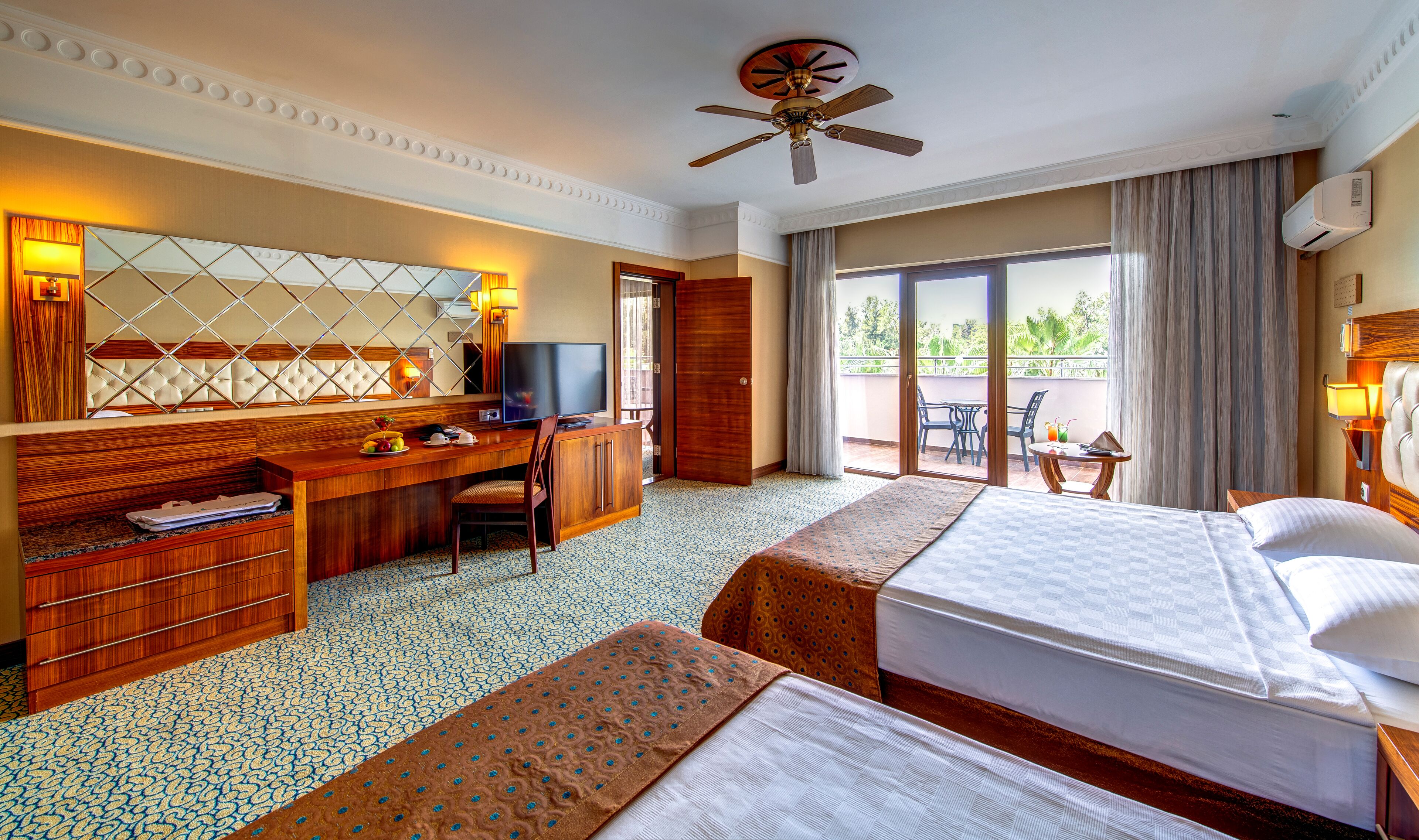 Habitación de hotel con cama, escritorio, silla, televisión y un balcón con mesa y sillas.