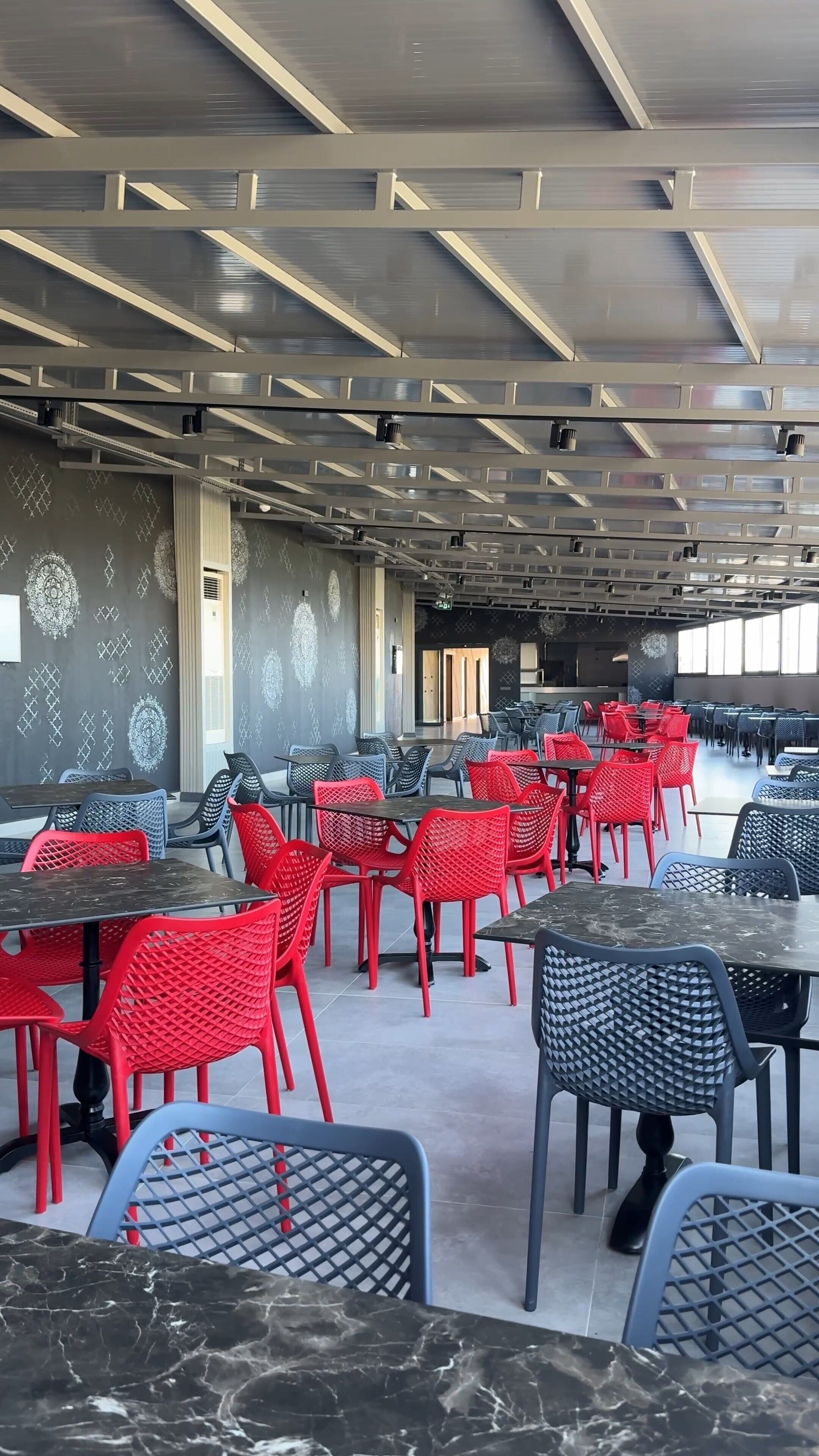 Un comedor amplio con techos altos, paredes con diseños y diferentes opciones de asiento, incluyendo sillas rojas y negras.