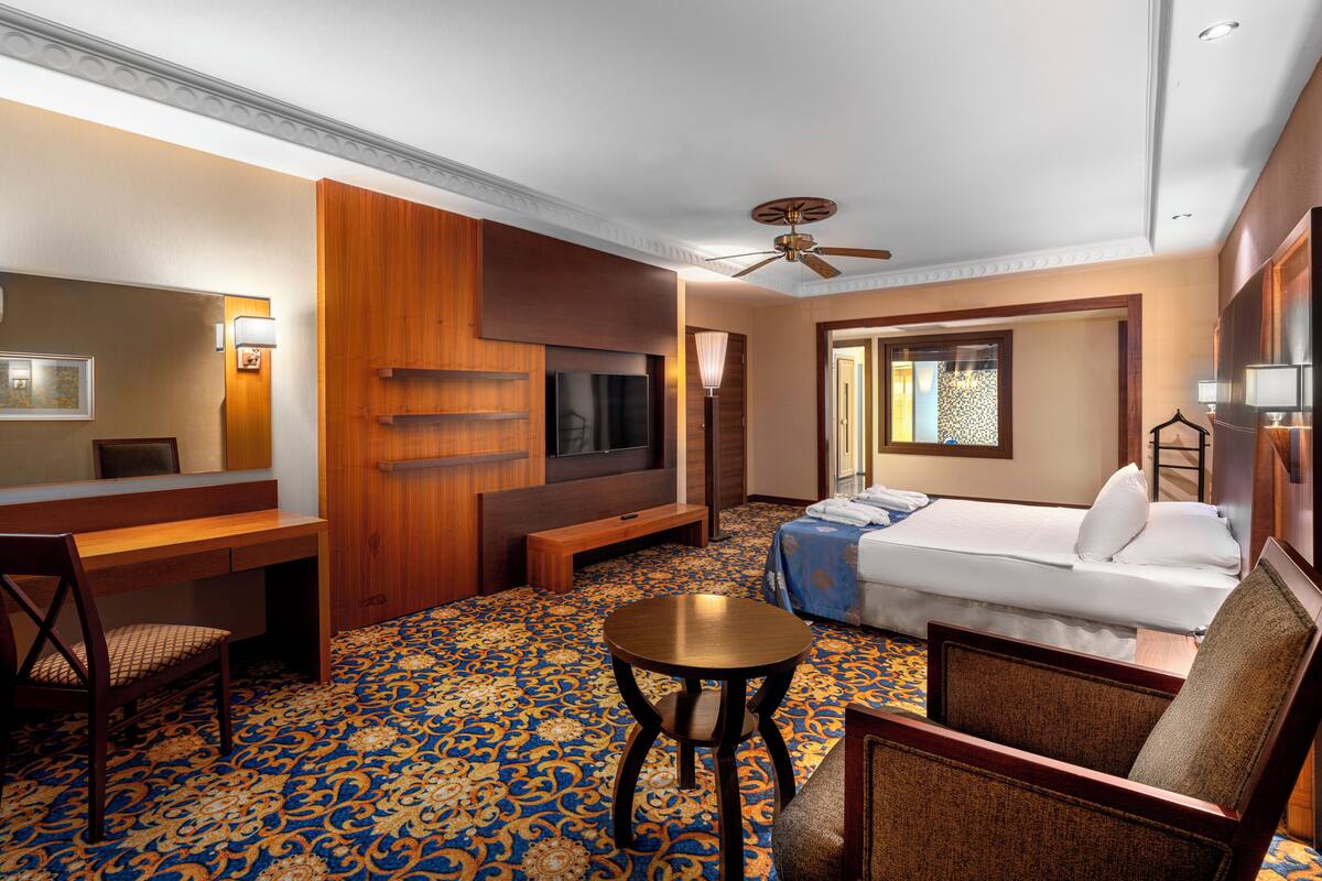 A hotel room with a bed, a desk, a chair, a TV, and a ceiling fan.