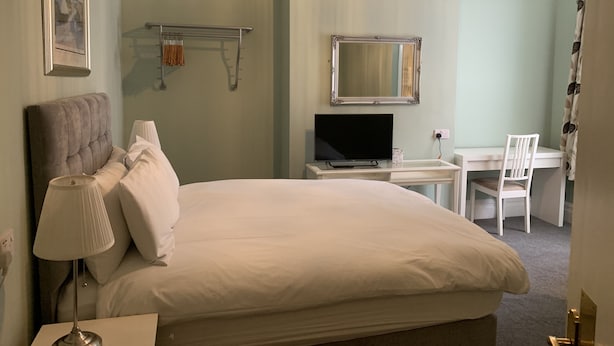 Habitación de hotel con cama, escritorio, silla, televisor, espejo y candelabro.
