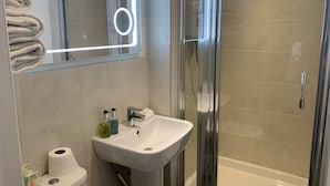 Un baño moderno con ducha de vidrio, lavabo blanco y espejo con luz circular.