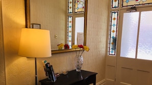 Una habitación con una mesa negra, una lámpara y un florero con flores. Hay vidrieras y un espejo en la pared.