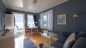 A room with a blue patterned wall, a white ceiling, a blue sofa, a white table, and a window with curtains.