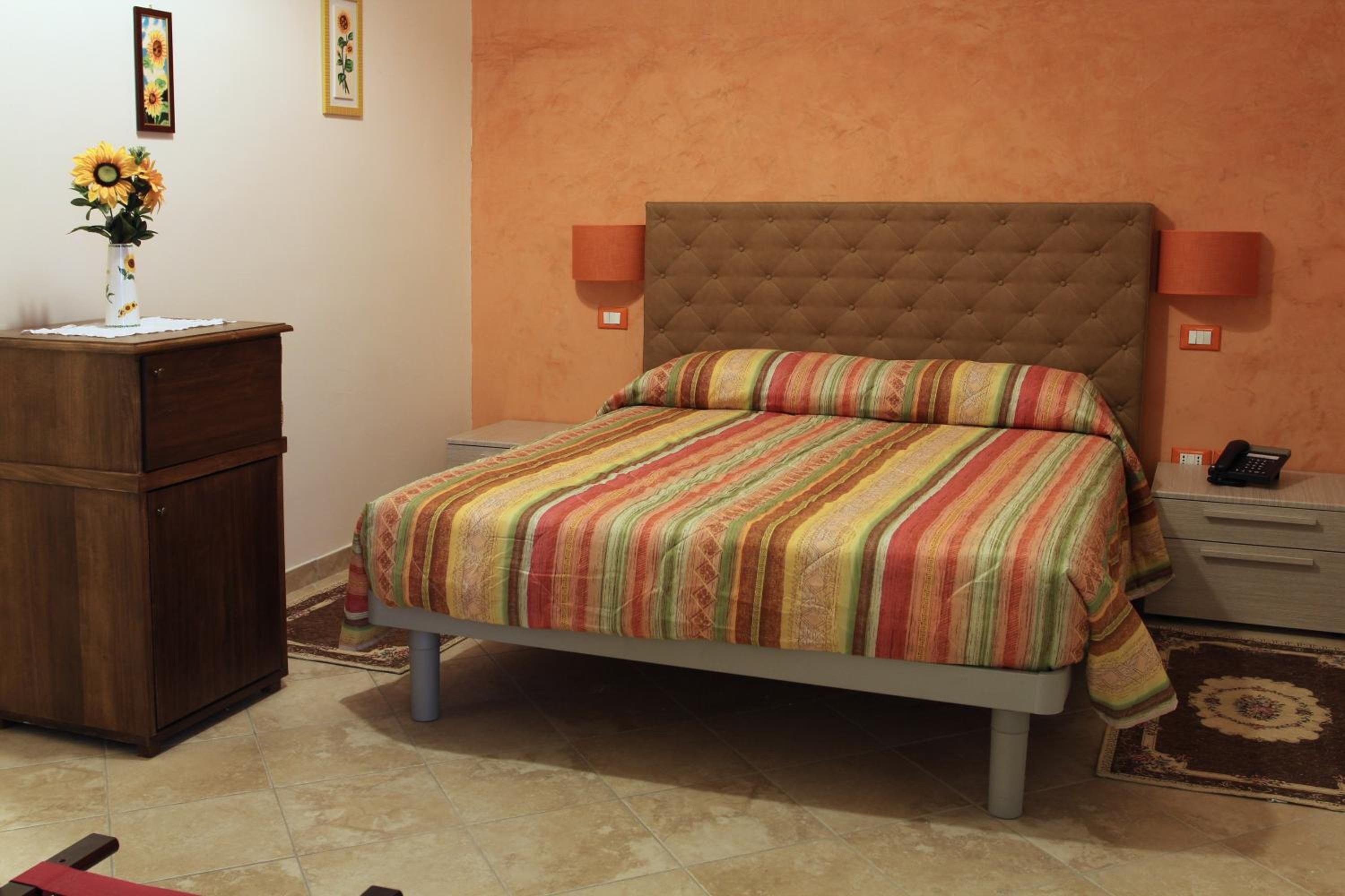 Una camera da letto con un letto, un comodino, una cassettiera e un vaso di girasoli.