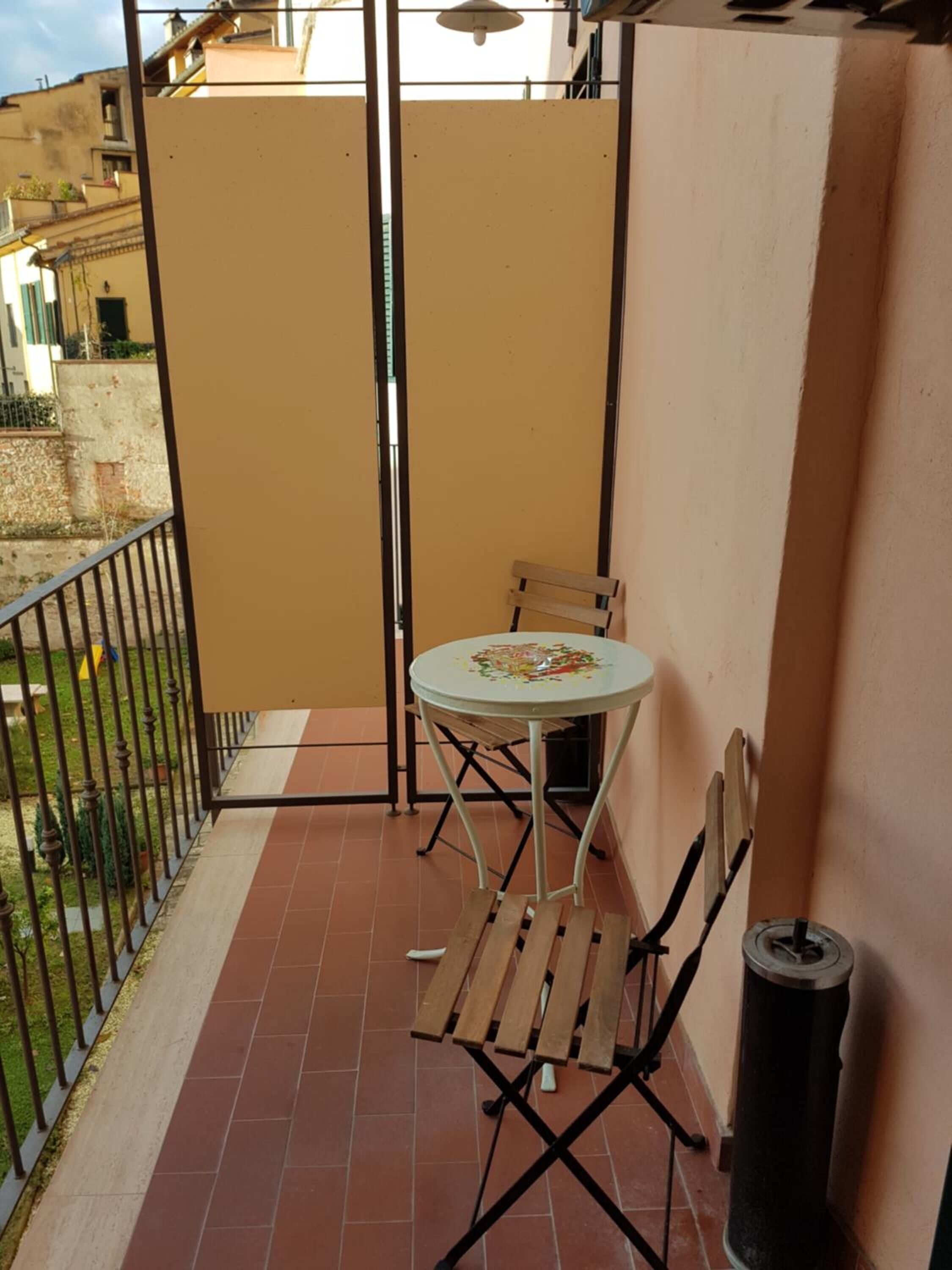 Een balkon met een kleine tafel en stoelen, een prullenbak en uitzicht op de omliggende gebouwen.