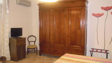 Une chambre avec une armoire en bois, un téléviseur posé sur une petite commode, une chaise et un lit recouvert d’une couverture à rayures.
