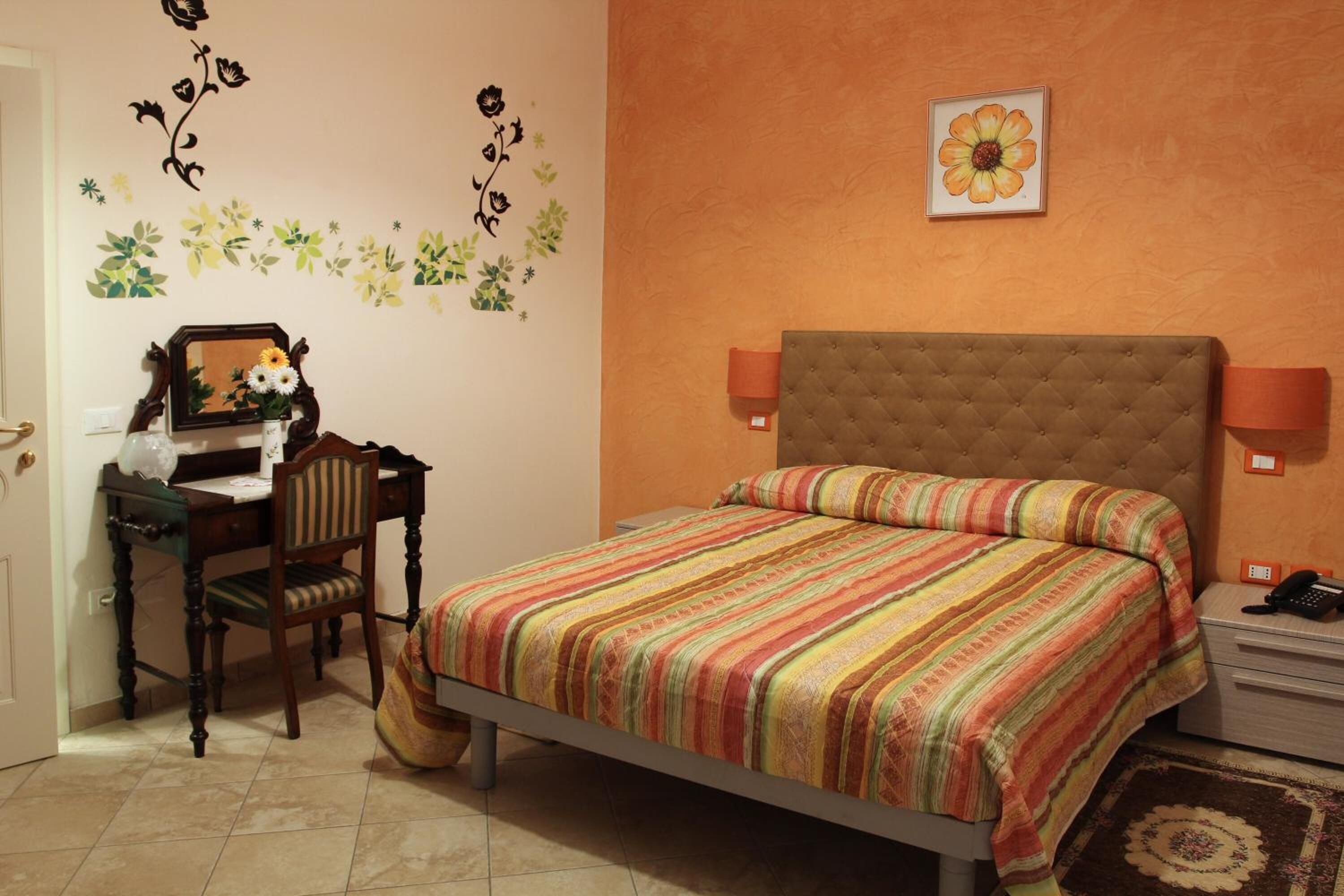 Un dormitorio con cama, escritorio, silla y pared decorada con motivos florales.