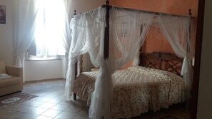 A four-poster canopy bed with a floral bedspread, a wooden headboard, and a view of a window with curtains. - Locanda dei Fiori (Pistoia)