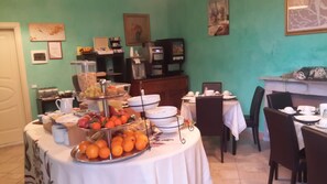 A dining area with a buffet table featuring fruits and pastries, a coffee machine, and a television. - Locanda dei Fiori (Pistoia)
