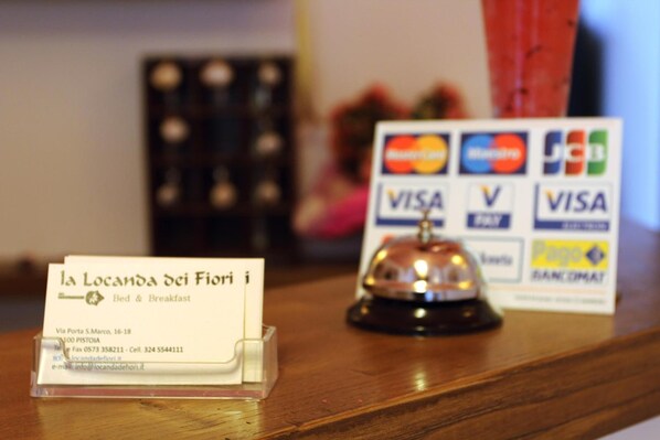 A hotel reception desk with a business card holder displaying the name 'la Locanda dei Fiori' and contact information. - Locanda dei Fiori (Pistoia)