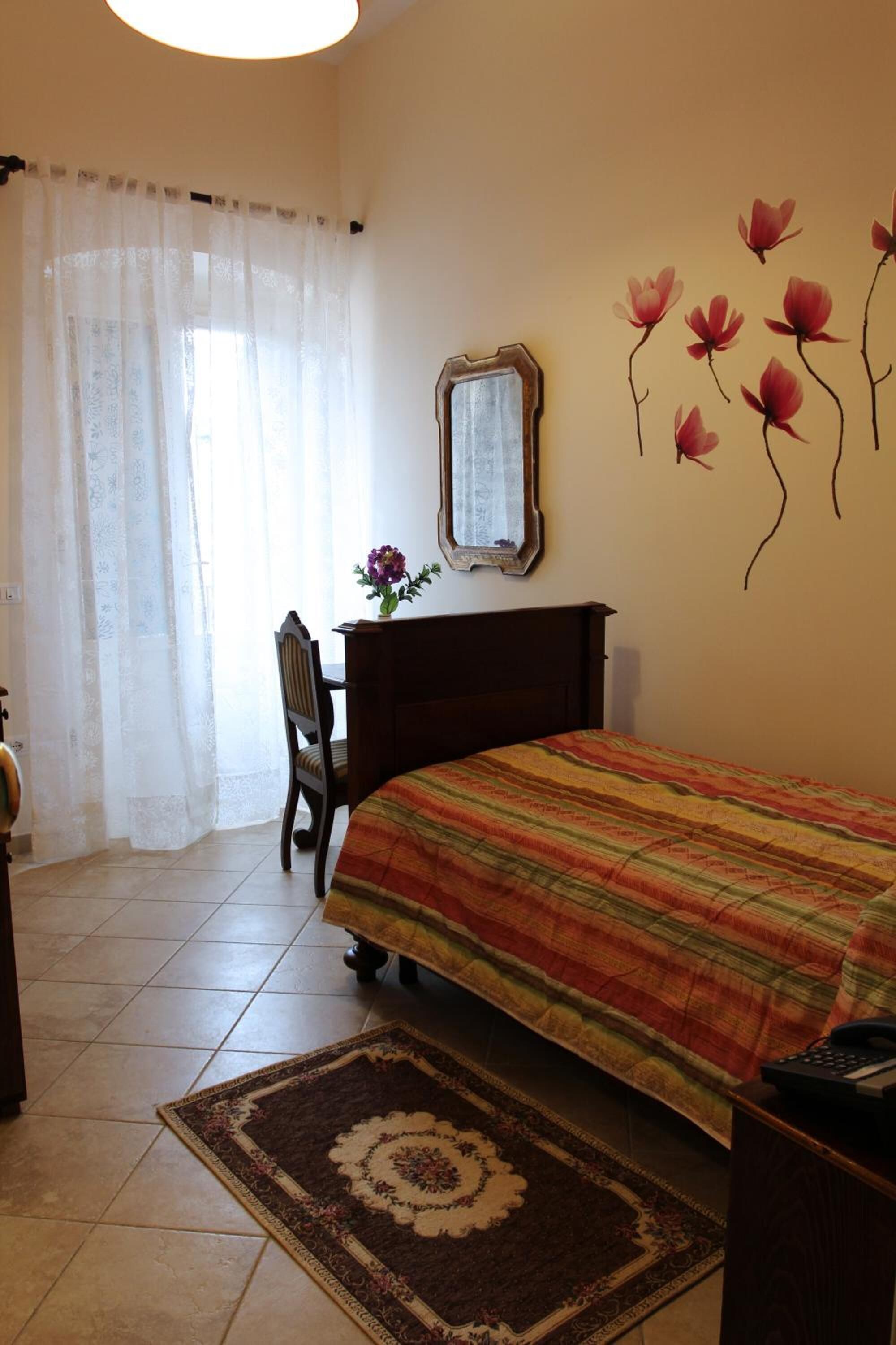 A bedroom with a bed, a desk, a chair, a mirror, and a wall with floral decals.