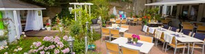 Un patio al aire libre con mesas y sillas, rodeado de follaje y flores.