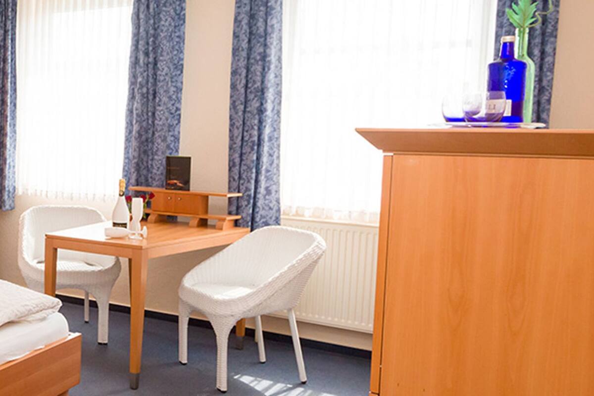 A hotel room with a bed, a desk, a chair, a wardrobe, a lamp, and a painting on the wall.